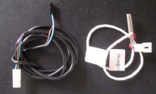 Zwei Hochtemperaturfühler mit verschiedenen Kabeln. Links ein schwarzes Kabel, rechts ein weißes Kabel mit einem metallischen Sensor. Beide Komponenten stammen von Remeha.